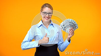 Beautiful business woman showing thumbs up holding money, well paid job, income Stock Photo