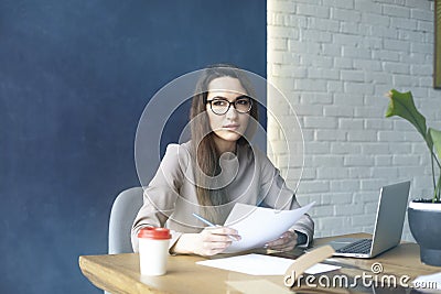 Beautiful businesswoman with long hair working with documentation, sheet, laptop while sitting in modern loft office. Stock Photo