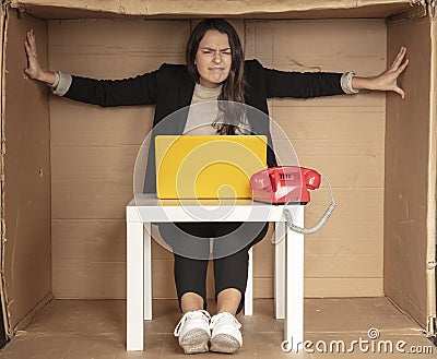 Beautiful businesswoman sits in a tight paper office, needs more space, pushes the walls Stock Photo