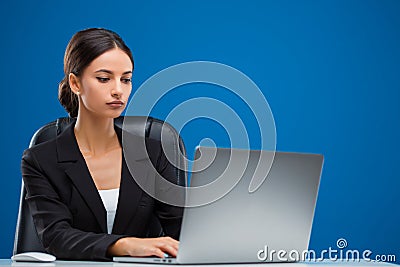 Beautiful businesswoman sitting at her desk working on her laptop, isolated on blue background Stock Photo