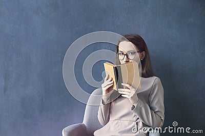 Beautiful businesswoman sitting in loft office reading vintage book. Look into opened book brown cover. Dark blue wall background Stock Photo