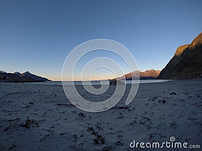 Beautiful calm blue waves hitting white frozen sandy beach in late autumn in the arctic circle with deep mountain and open sea vie Stock Photo