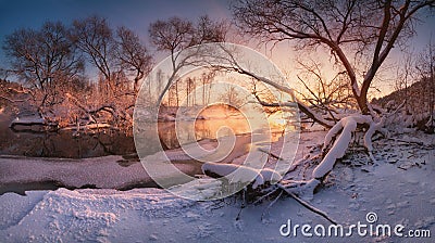 Beautiful calm evening on the small winter river, surrounded by overhanging trees. Winter landscape with a frozen river Stock Photo