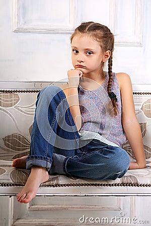 Beautiful calm thinking unhappy kid girl sitting on the bench in Stock Photo