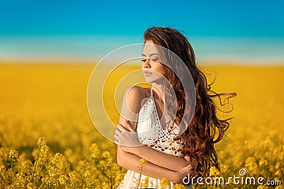 Beautiful carefree girl with long curly healthy hair over Yellow rape field landscape background. Attracive brunette with blowing Stock Photo