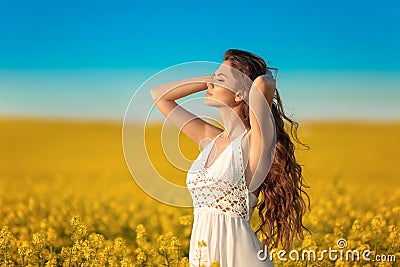 Beautiful carefree girl with long curly healthy hair over Yellow rape field landscape background. Attracive brunette with blowing Stock Photo