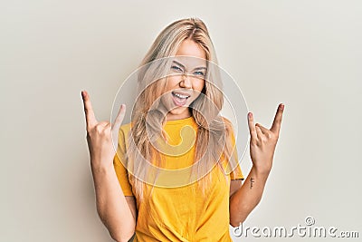 Beautiful caucasian blonde girl wearing casual tshirt shouting with crazy expression doing rock symbol with hands up Stock Photo