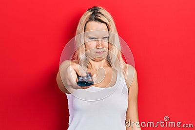 Beautiful caucasian blonde woman holding television remote control skeptic and nervous, frowning upset because of problem Stock Photo