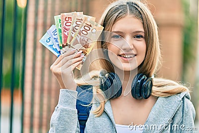 Beautiful caucasian student teenager using headphones holding canadian dollars at the city Stock Photo