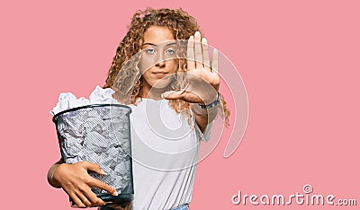 Beautiful caucasian teenager girl holding paper bin full of crumpled papers with open hand doing stop sign with serious and Stock Photo