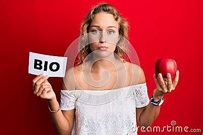 Beautiful caucasian woman holding red apple and bio word depressed and worry for distress, crying angry and afraid Stock Photo