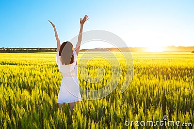 Beautiful caucasian woman in white dress jumping up with raised hands outdoor. Field with yellow wheat around Stock Photo