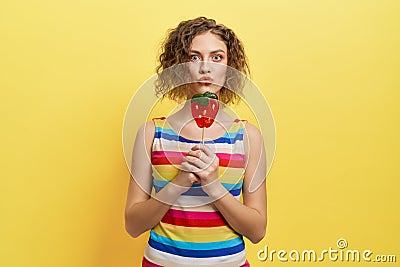 Playful girl in striped dress holding berry lollipop. Stock Photo