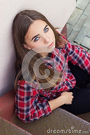 Beautiful charming young attractive girl with large blue eyes with dark long hair in autumn day sitting on the stairs Stock Photo