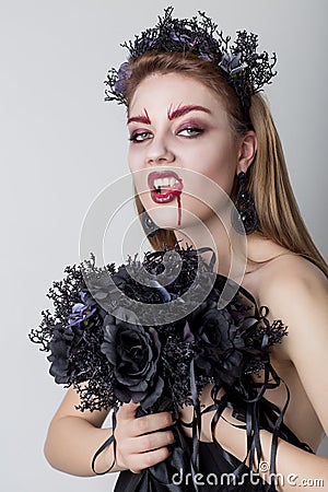 Beautiful cheeky girl in the image of a vampire with bright dark makeup, black vampire bride with a bouquet and a black wreath Stock Photo
