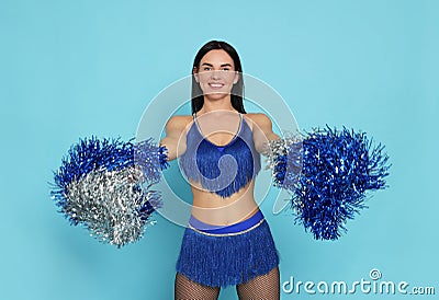 Beautiful cheerleader in costume holding pom poms on light blue background Stock Photo