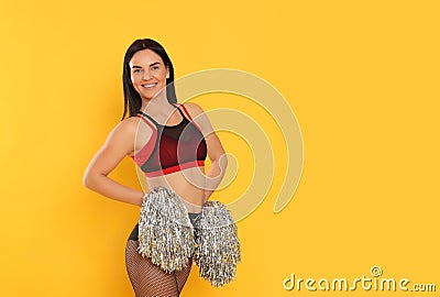 Beautiful cheerleader in costume holding pom poms on yellow background. Space for text Stock Photo