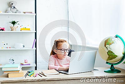 beautiful child in eyeglasses using laptop while studying at desk Stock Photo