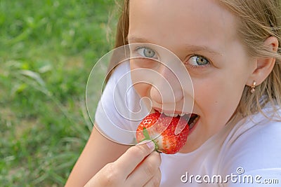 A beautiful child with green eyes is eating strawberries in her hands and smiles Stock Photo