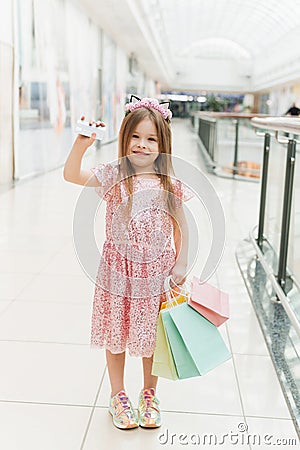 A beautiful child in the mall makes shopping. Online shopping concept. A girl in a pink dress with multi-colored pastel bags in Stock Photo