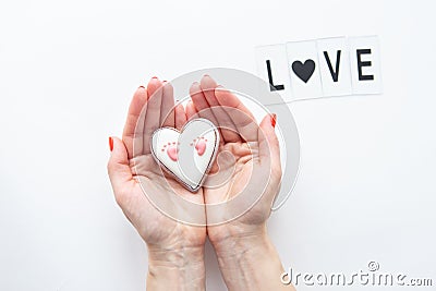 Beautiful children`s footprint in the shape of a heart, the girl`s hands hug the heart. Love lettering Stock Photo