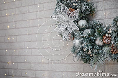 Beautiful Christmas wreath of fir branches, cones, white baubles, flowers, berries and icycles on brick wall with garland lights. Stock Photo