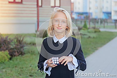 Beautiful and clever blonde kid girl solves a cube puzzle, outside near school. Editorial Stock Photo