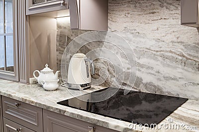 beautiful closeup of custom designed kitchen, with marble looking quartz countertop and backsplash. cream electric kettle with Stock Photo