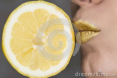 Beautiful closeup with female lips with gold color makeup and lemon slice. KIss. Glitter cosmetics Stock Photo