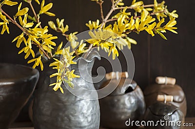 Beautiful closeup of unique handmade pot with wooden detail and branches of Forsythia in black vase Stock Photo