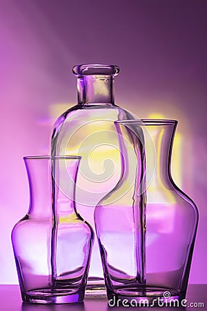 Glass transparent tableware - bottles of different sizes, three pieces on a beautiful multi-colored, yellow, lilac and Stock Photo