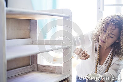 Beautiful concentrated lady at work at home restyling and repairing an old furnitre with white paint. do it yourself indoor Stock Photo