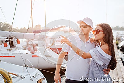 Beautiful and confident couple stands on pier and hug each other. They stand very close. Girl point with finger. They Stock Photo