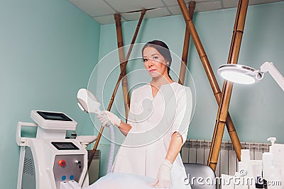 Beautiful cosmetician in medical gloves is showing her workplace, looking at camera and smiling. Stock Photo