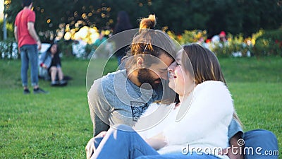 Beautiful couple caressing sitting on green grass in park. Concept. Happy young couple hugging on green grass in sun Stock Photo