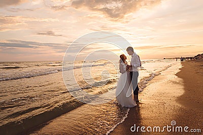 A beautiful couple of newlyweds, the bride and groom walking on the beach. Gorgeous sunset and sky. Wedding dresses, a Stock Photo