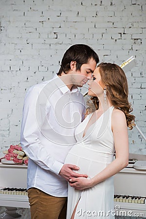 Beautiful couple, pregnant young woman and man hugging with love, on piano background. Stock Photo