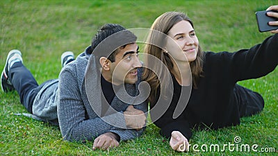 Beautiful couple takes selfie lying on green grass. Media. Young man and woman are photographed on phone lying on grass Stock Photo