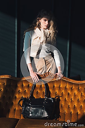 beautiful curly blond hair woman posing with a small black shopper bag near vintage volor sofa Stock Photo
