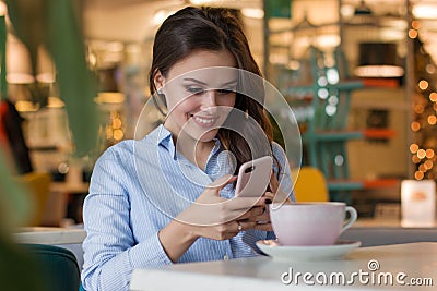 Beautiful cute caucasian young woman in the cafe, using mobile phone and drinking coffee smiling Stock Photo