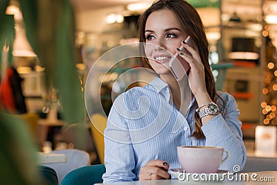 Beautiful cute caucasian young woman in the cafe, using mobile phone and drinking coffee smiling Stock Photo