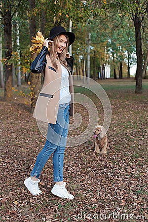 Beautiful cute cheerful girl in a black hat with a bouquet of bright colored leaves in a coat walks in autumn park Stock Photo
