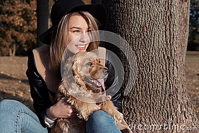 Beautiful cute happy girl in a black hat playing with her dog in a park Stock Photo