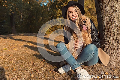 Beautiful cute happy girl in a black hat playing with her dog in a park in autumn another sunny day Stock Photo