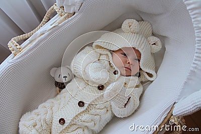Beautiful 2 month old baby girl in a white knitted suit lies in her white crib Stock Photo