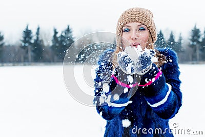 Beautiful cute playful happy young woman in a blue coat in the cap playing with snow in the park Stock Photo