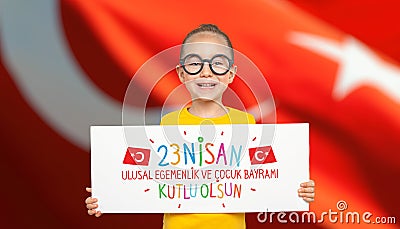 Beautiful cute Turkish girl holding a white paper with national holiday celebration message in front of turkey flag. 23 Nisan Kutl Stock Photo