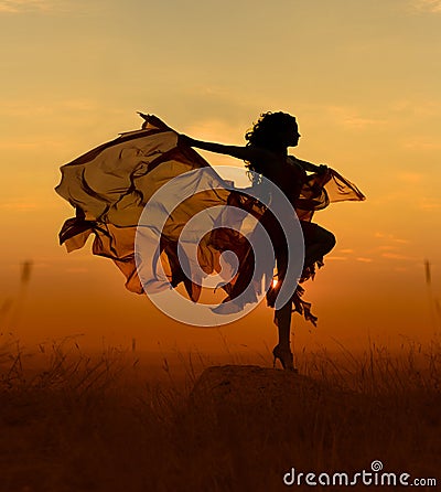 Beautiful dancer woman with flying dress and veil at sunst, orange background. Stock Photo