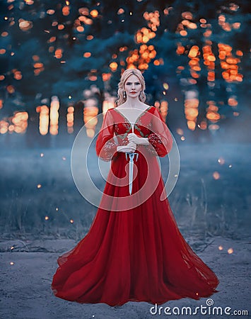 Beautiful, dangerous blonde queen in a red fashion lush dress with a dagger in her hands. Backdrop dark fantasy forest Stock Photo