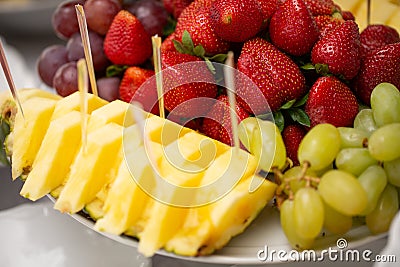 Decorated various fruits on plate at restaurant, wedding catering. Pineapple, strawberry, green grape. Stock Photo